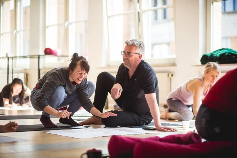 Yoga students laughing and working together in a bright studio.